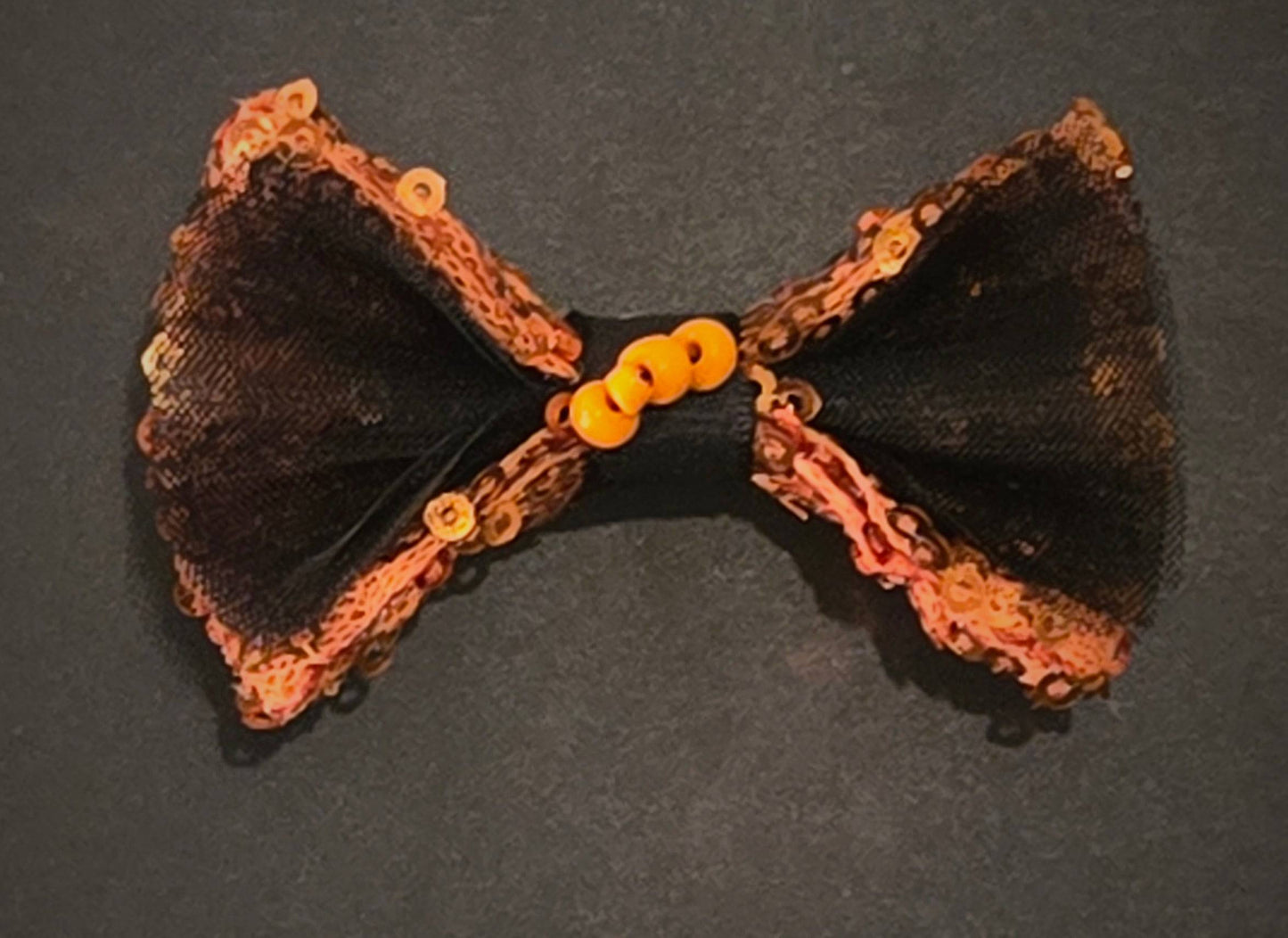 A close up at hair bow. made of matching pumpkin sequin fabric and black tulle. Hand embroidery at center. 