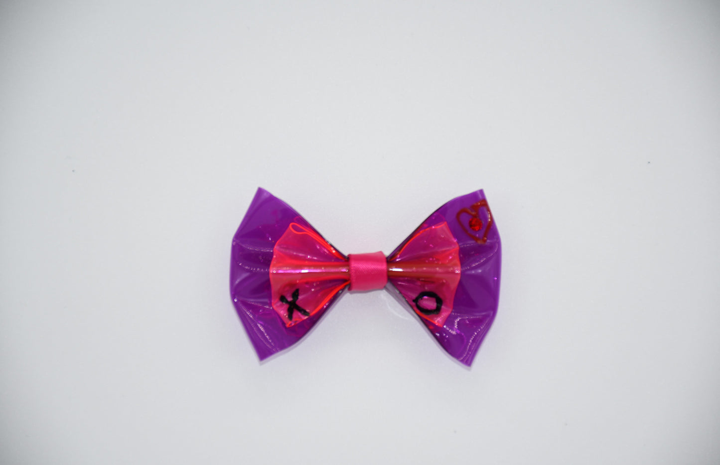 XOXO Mister Fashion Pet Hair Bow. All items are Limited Quantity. Made of a hot pink and orchid clear vinyl fabric. Carefully hand placed red crystal in the center of the heart. Hand Painted heart and XO. Hot pink ribbon. Hair bow measures 3 inches wide and 2 inches tall.